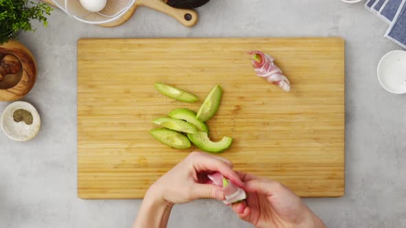 Crop person wrapping avocado with bacon during dinner preparation in kitchen