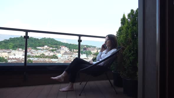 Concentrated Lady in Glasses Talks on Smartphone Sitting on Terrace