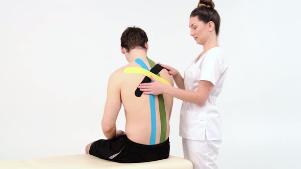 Physiotherapist sticks kinesio tapes to the back of patient, kinesiology taping, kinesiological 
