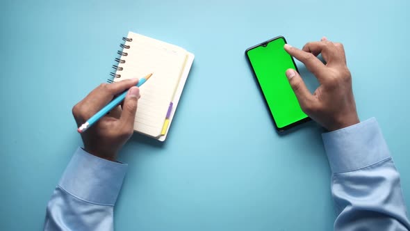 Man Hand Using Smart Phone and Writing on Notepad