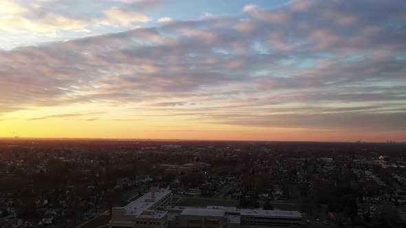An drone view of a Long Island neighborhood during a golden sunrise with clouds and blue skies. The