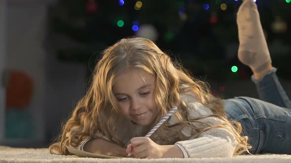 Pretty Girl Writing Letter to Santa, Closing Her Eyes With Hands to Image Gifts