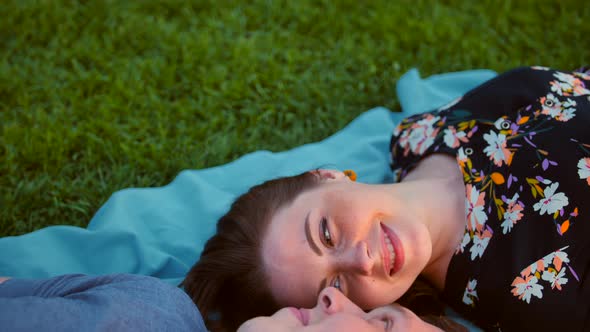 Happy Young Adult Couple Lying on the Grass Over Sunrise. Teal and Orange.