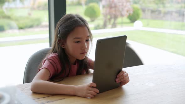 Concentrated Asian girl typing on tablet alt