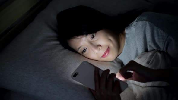 Woman working on cellphone and lying on bed at night