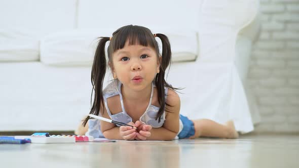 Cute adorable asian ethnic kid girl holding color pen drawing and painting, lying on warm floor, She alt