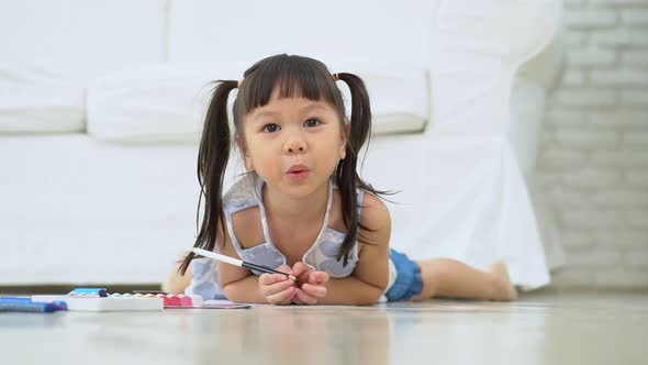 Cute adorable asian ethnic kid girl holding color pen drawing and painting, lying on warm floor, She