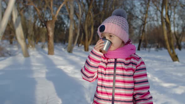 Smiling Child Kid Girl Drinking Hot Drink Tea From Cup Trying to Keep Warm in Winter Park Forest