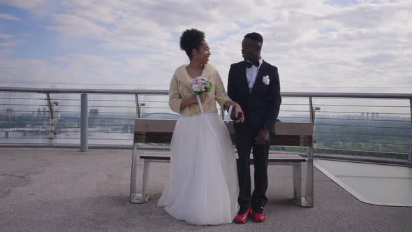 Wide Shot of Happy Newlyweds Talking Standing at Bench on Bridge Smiling