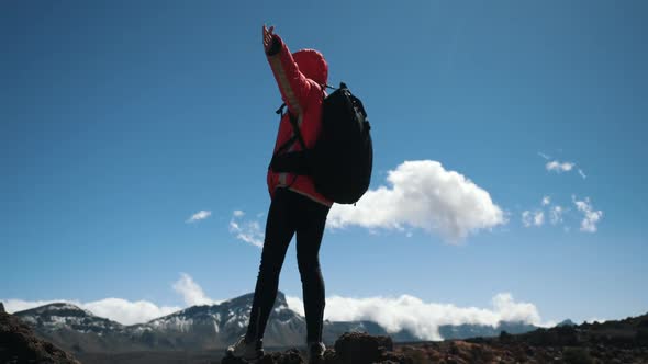 Young Woman Hiker with Black Backpack Arms Outstretched Stays on the Summit High in Mountains