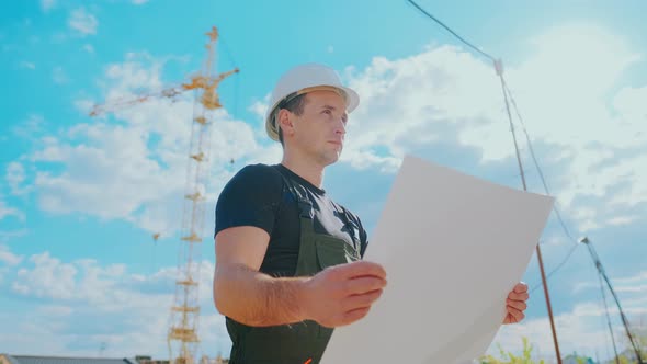 A Man in a Helmet Is Holding a Construction Plan in His Hands. A Builder Is Checking Blueprints.