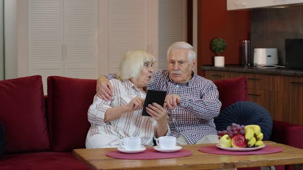 Senior Pensioner Couple with Digital Tablet Pc Computer at Home. Resting on Sofa in Cozy Living Room