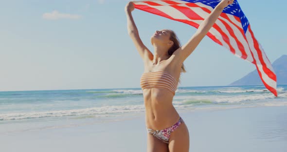 Front view of young Caucasian woman holding a American flag on the beach 4k