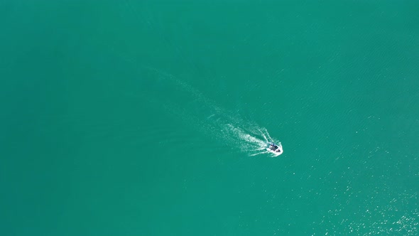 Drone flight over a motor boat in turquoise green sea.