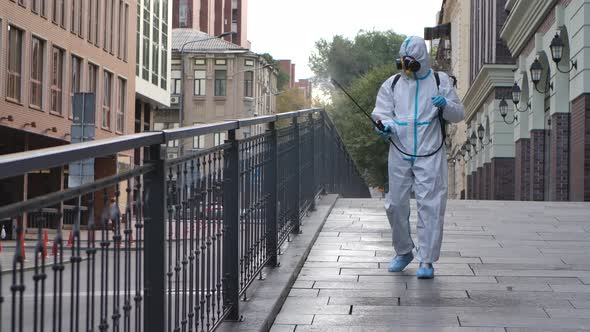 A Working Man in a Protective Suit and a Respirator Disinfects, Sprays Chemicals on the Surface of