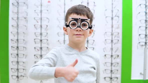 Little Boy Stands on a Background of a Showwindow with Frames for Spectacles with the Device 