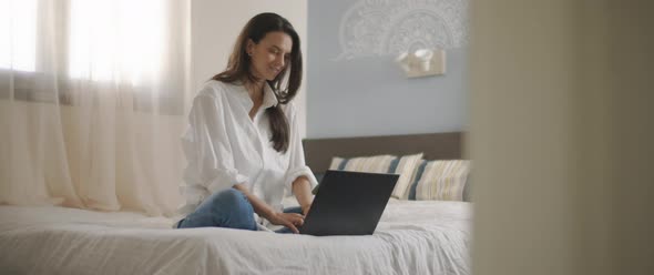 A young woman smiling while working on her computer from home.