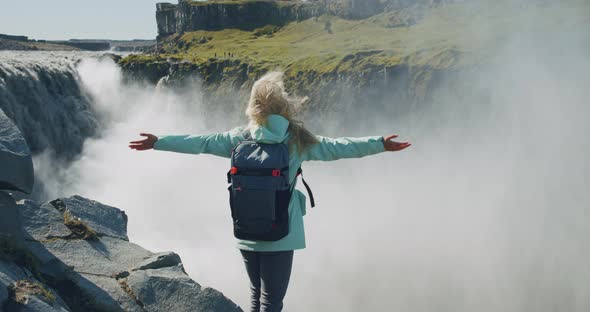 Woman Standing on the Edge of the Cliff and Raising Her Hands Up in the Air Wiht Beautiful Detifoss