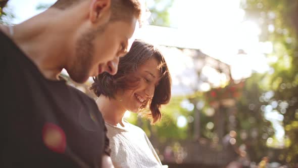 Young Beautiful Couple Smiling Speaking Looking at Tablet Sitting in City Park