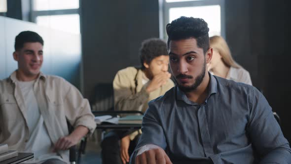 Young Excited Arab Guy Student Sitting in Classroom Cannot Concentrate on Lesson Being Ridiculed By