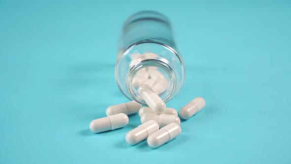 Medicinal capsules spilled out of a glass bottle on a blue bright table