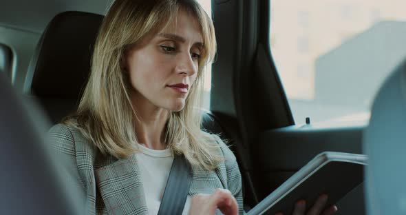 Businesswoman Sitting in Back Seat of Taxi or Car Working on Digital Tablet