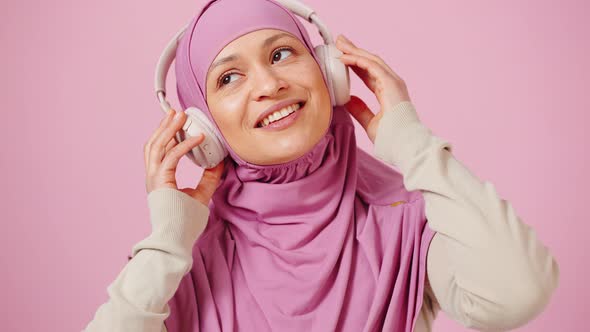 Portrait of Muslim Lady in Hijab Enjoying Music in Headphones Dancing Over Pink Studio Background