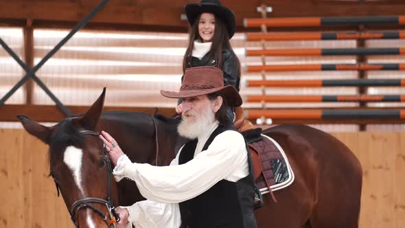 Senior Man Assisting Granddaughter Horseback Riding in Ranch