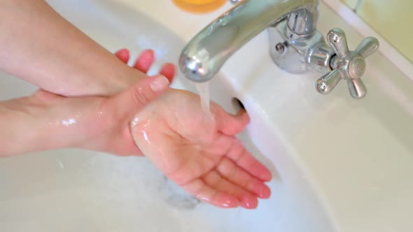girl washes her hands with soap in the bathroom over the sink next to flowing water.
