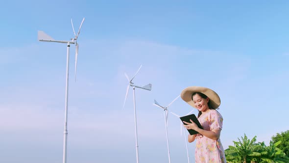 Asian young woman using a digital tablet in the field in the background wind power production turbin