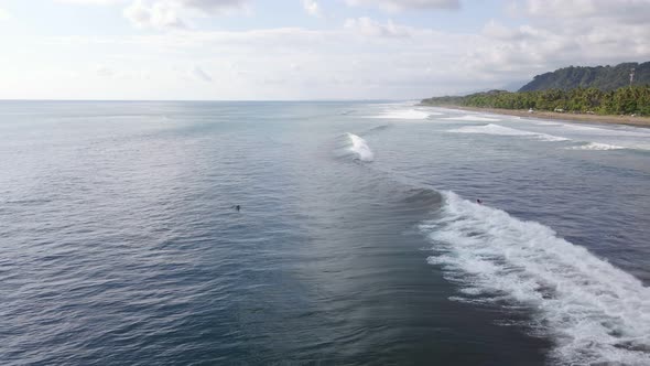 Two surfers catching waves at Dominical Beach in Costa Rica on a cloudy day. Stationary aerial view