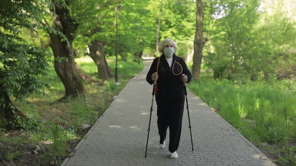 Active Senior Old Woman in Mask Training Nordic Walking in Park at Quarantine