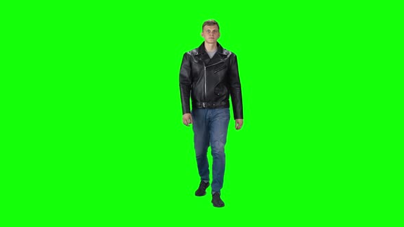 Young Man in Black Leather Jacket, Jeans and Sneakers Going Against a Green Background. Slow Motion.