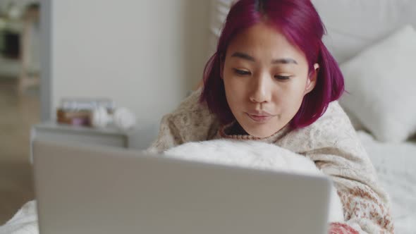 Young Asian Woman Lying on Bed and Using Laptop