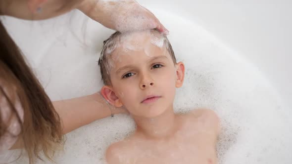 Portrait of Smiling Little Boy Looking at Mother While She Washes His Hair with Shampoo in Bathroom