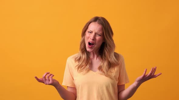 Displeased blonde woman wearing yellow t-shirt saying what at the camera