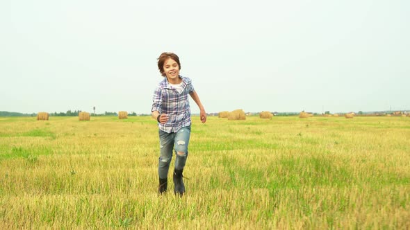 Smiling Boy Teenager Running on Harvesting Field on Haystack Background in Village