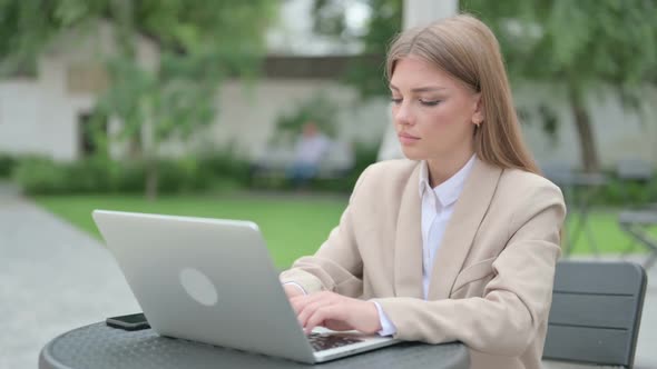 Young Businesswoman with Laptop Pointing at Camera in Outdoor Cafe