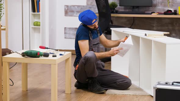 Male Worker Talking on the Phone While Assembles White Furniture