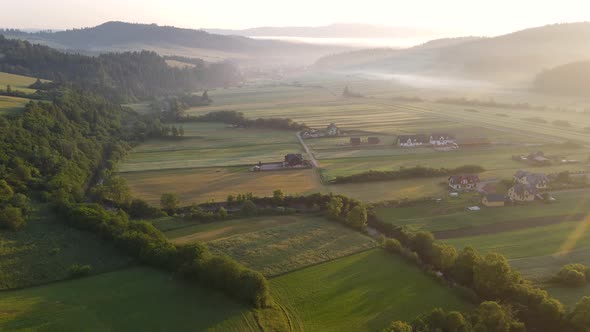 Aerial drone fly over farm fields and Kacwin village in Polish mountains at sunrise.