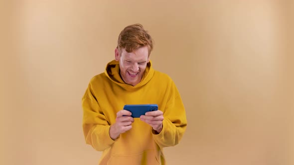 Nice Addicted Cheerful Guy Using Gadget Playing Network Game on a Beige Background