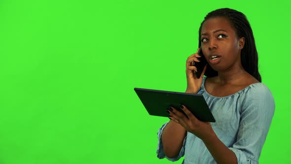 A Young Black Woman Talks on a Smartphone While Holds a Tablet - Green Screen