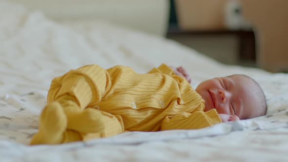 Newborn Baby Sleeps on His Back with His Arms Up and Smiles in His Sleep