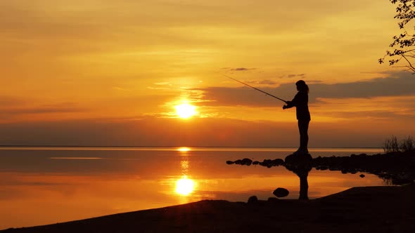 Woman Fishing on Fishing Rod Spinning at Sunset Background.