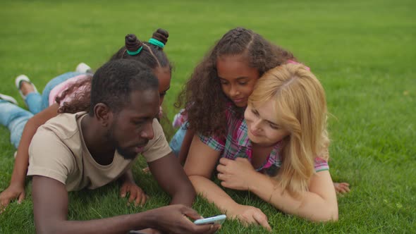 Multiethnic Family with Cellphone Lying on Grass