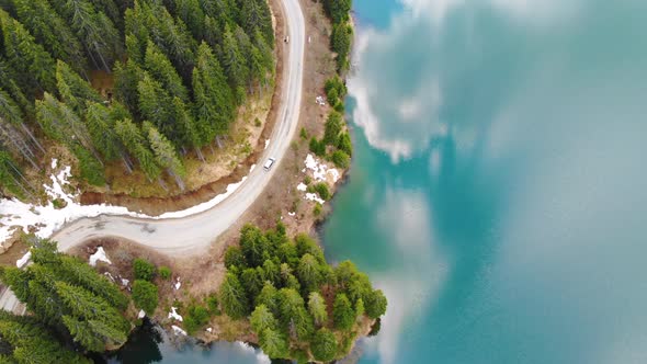 Aerial view of car driving through the forest and the lake on the side. Beautiful mountain road.