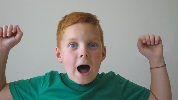 Adorable Handsome Redhaired Boy with Freckles Looking Into Camera and Raise Hands Rejoicing