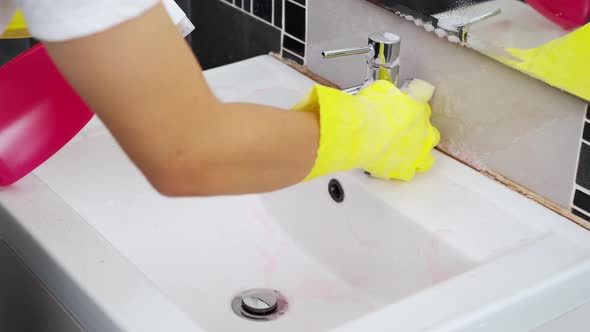 hand cleaning bathroom sink with spray detergent and sponge