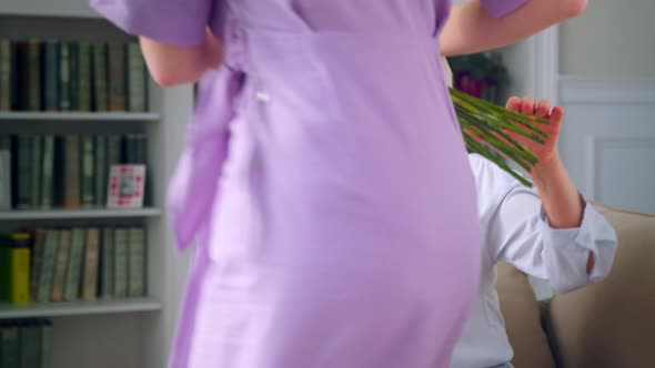 A young blonde woman giving red roses to an elderly mother on mother's day