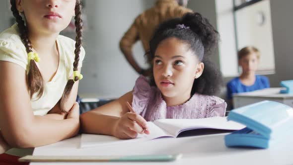 Video of happy diverse girls at desk doing lessons together in classroom